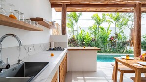Eine moderne Küche mit Marmorarbeitsplatte, Holzregalen und Blick auf einen Pool und tropische Pflanzen.