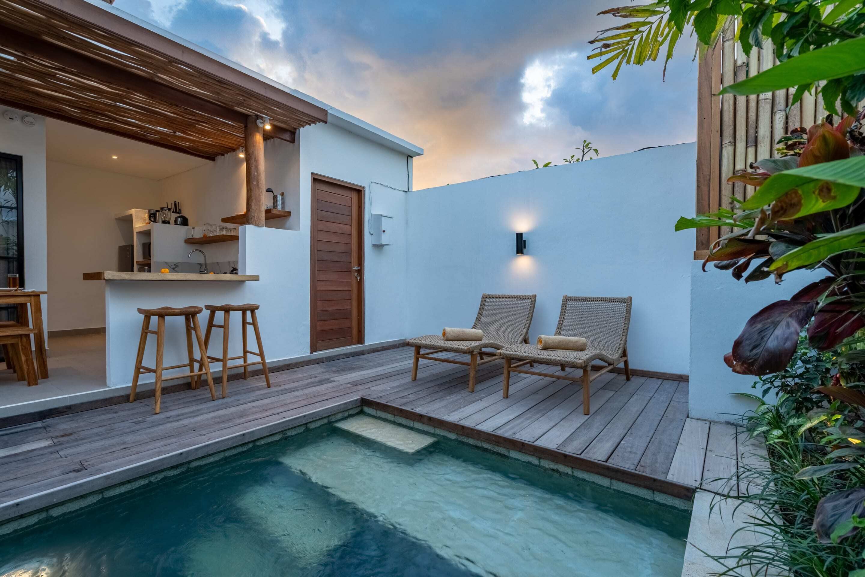 A modern outdoor pool area with wooden deck, lounge chairs, and a bar area with stools.
