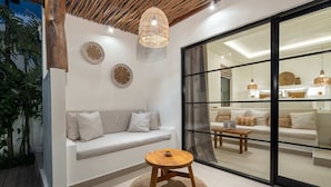 Ein modernes Wohnzimmer mit Holzboden, einem weißen Sofa, einem runden Holztisch und einer Glastür zu einem anderen Raum.