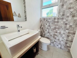 Un baño con lavamanos blanco, inodoro y paredes con azulejos estampados.