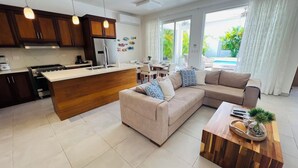 A modern living room with a beige sofa, a wooden coffee table, and a kitchen area with wooden cabinets and a central island.