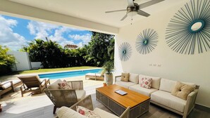 A modern outdoor living area with a pool, wicker furniture, and decorative wall art.