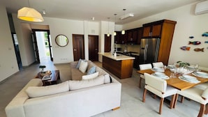 A modern kitchen with dark wooden cabinets, a stainless steel refrigerator, and a dining area with a wooden table and white chairs.