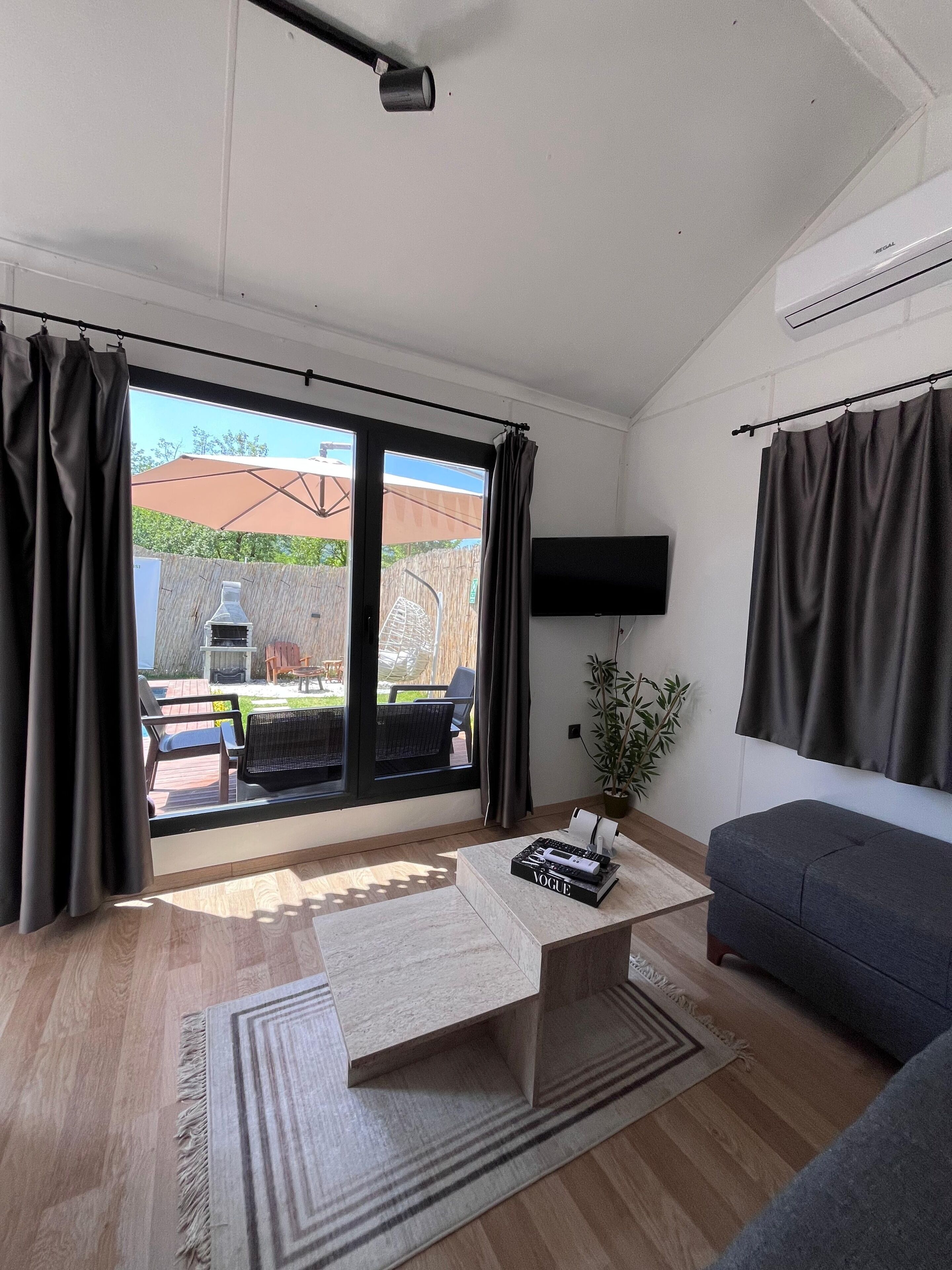 A modern living room with a sofa, a coffee table, a TV mounted on the wall, and a sliding glass door leading to an outdoor patio.