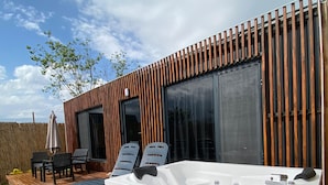 A modern outdoor hot tub area with a wooden deck, two lounge chairs, and a pool.