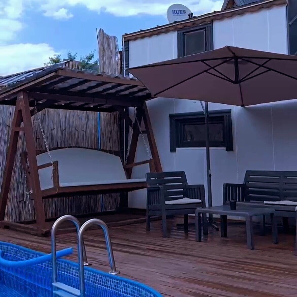 A pool area with a wooden swing, a covered seating area, and a table with chairs.