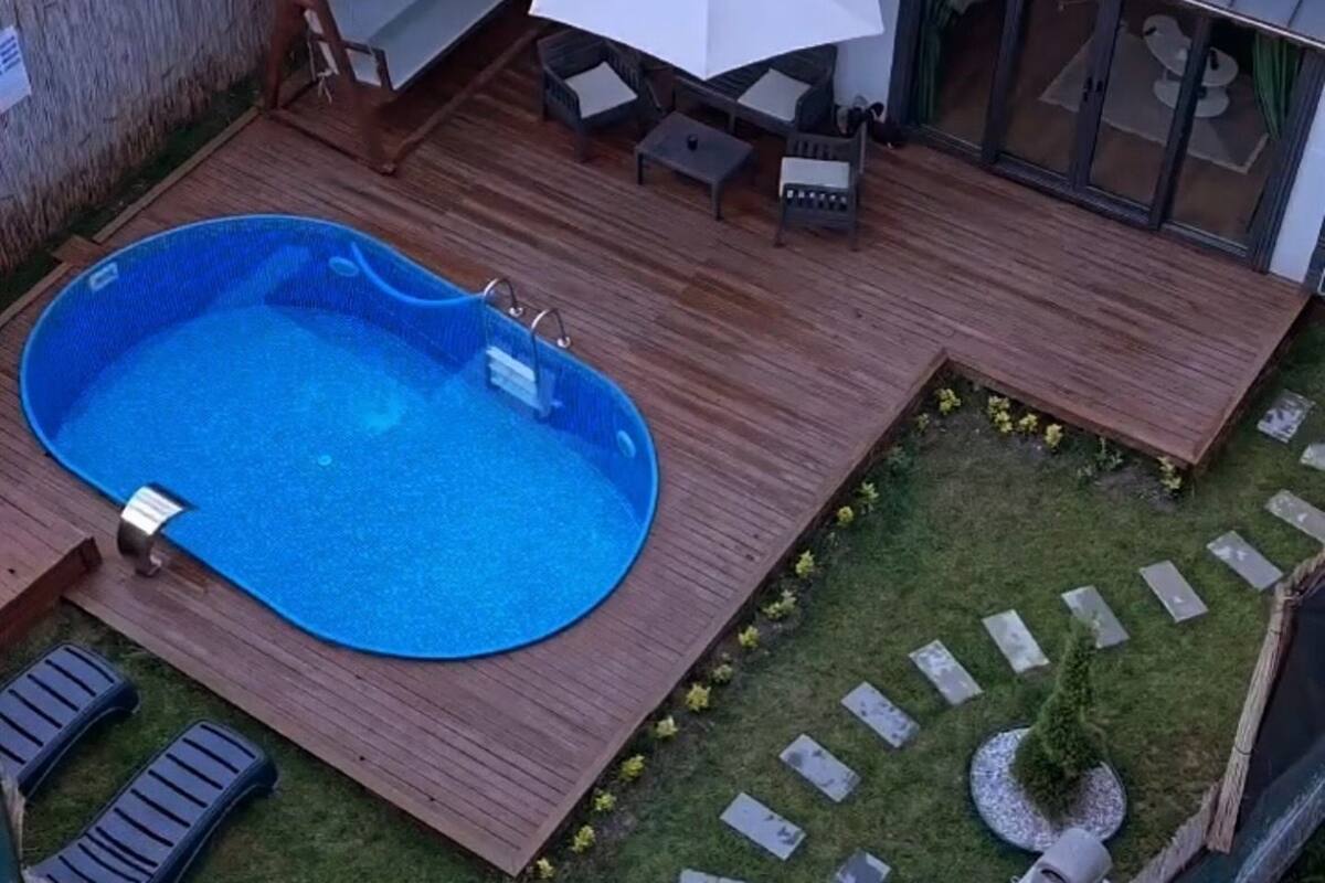 A backyard with a swimming pool, wooden deck, outdoor furniture, and a small garden.
