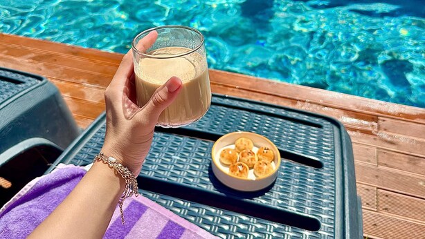 A person holding a glass of beverage by a poolside with a bowl of snacks.