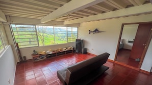 Una habitació amb una finestra gran, un sofà negre i una estanteria amb barrets.