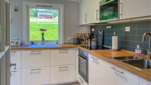A modern kitchen with white cabinets, a wooden countertop, a stainless steel sink, and a window with a view of a green field and a red barn. - Gorgeous home in Fiksdal with WiFi (Fiksdal)