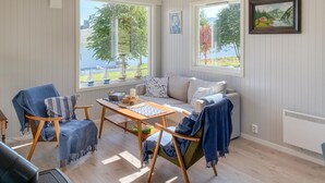 A cozy room with a wooden table, two chairs, a sofa, and large windows offering a view of trees and a lake. - Gorgeous home in Fiksdal with WiFi (Fiksdal)