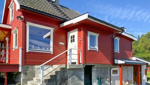A red building with a staircase leading to the entrance, a small porch area, and a visible window with a view of the sky. - Gorgeous home in Fiksdal with WiFi (Fiksdal)