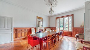 A spacious dining area with a large wooden table and multiple chairs, a chandelier, and large windows offering a view of the outdoors. - Pet friendly home in Chabris with WiFi (Chabris)