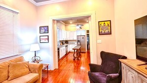 A living room with a sofa, a chair, a lamp, and a fireplace. There is a kitchen in the background with cabinets and a refrigerator. - Beautiful 3-bedroom house close to the Super Bowl and French Quarter! Book now (New Orleans)