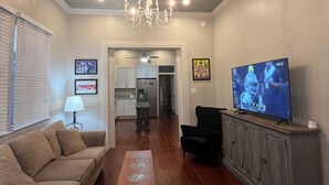 A living room with a wooden floor, a chandelier, a television, a sofa, a coffee table, and a cabinet. - Beautiful 3-bedroom house close to the Super Bowl and French Quarter! Book now (New Orleans)