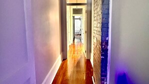 A hallway with wooden flooring, white walls, and a brick accent wall. - Beautiful 3-bedroom house close to the Super Bowl and French Quarter! Book now (New Orleans)
