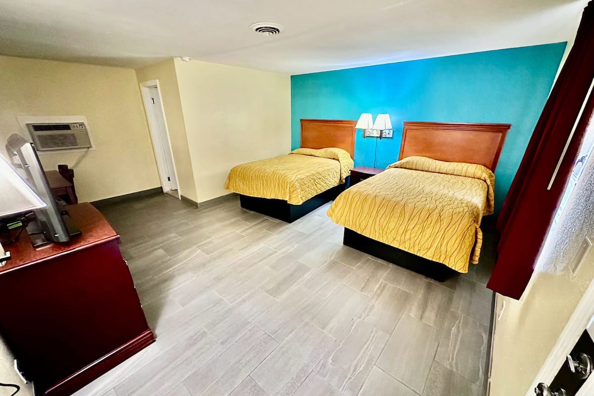 Quarto de hotel com duas camas, uma escrivaninha com computador e ar-condicionado fixado na parede.