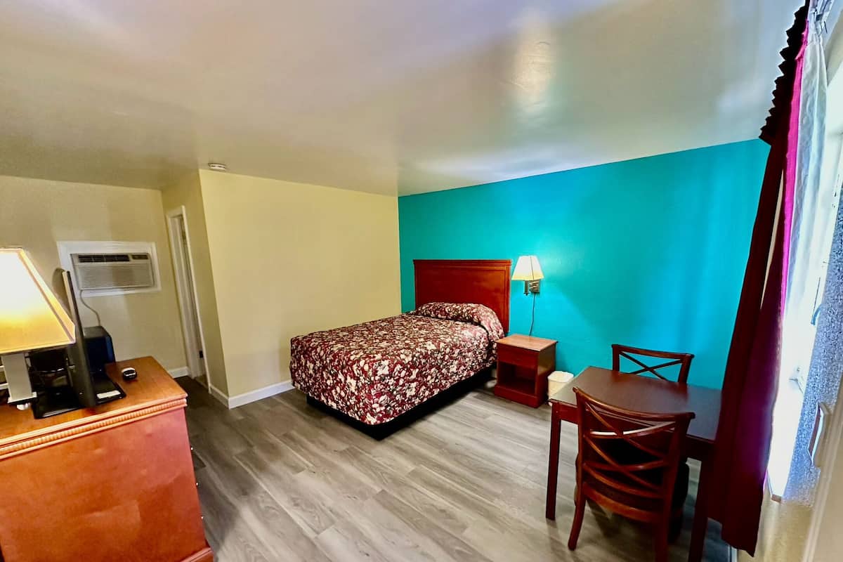 Quarto de hotel com cama, mesa de cabeceira, abajur e uma pequena escrivaninha com cadeira.