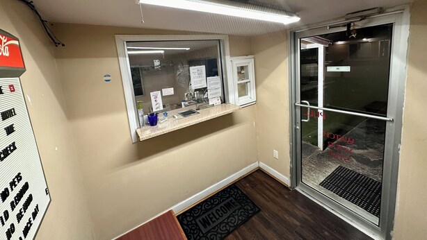 A room with a window, a reception desk, a door, and a ceiling light fixture. - Bel-Aire Motel Tuscaloosa (Tuscaloosa)