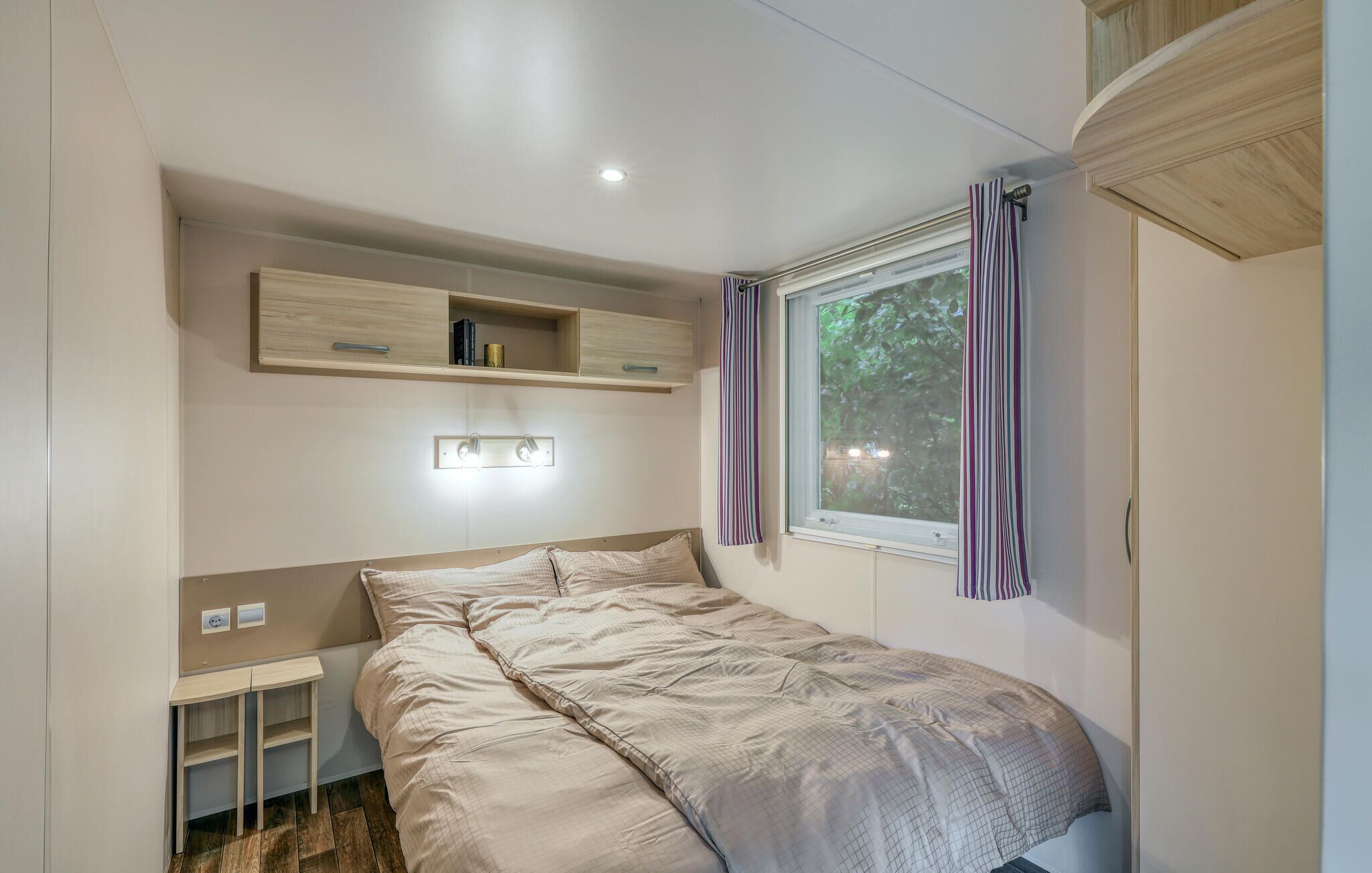 Une chambre à coucher comprenant un lit, une table de chevet, une étagère avec des livres, une fenêtre avec des rideaux et un luminaire au plafond.