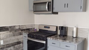 Cocina con gabinetes grises, estufa de acero inoxidable, microondas y cafetera.
