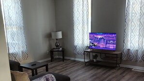 Una sala de estar con un sofá, una mesa de centro, un televisor sobre un mueble bajo y una lámpara en una mesita auxiliar.