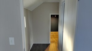 Un pasillo estrecho con suelo de madera, paredes blancas y una puerta que da a otra habitación.