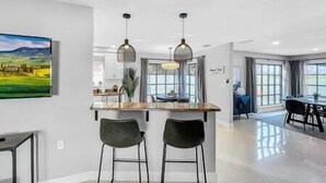 A modern kitchen with a bar area, two bar stools, and a dining area with a table and chairs.
