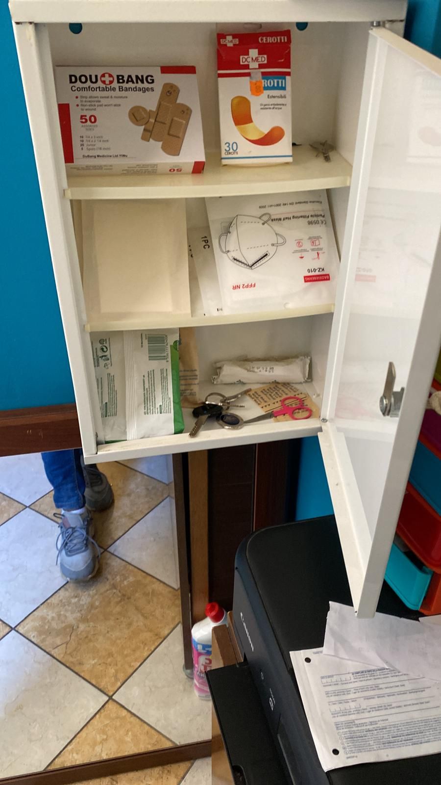 A storage cabinet with various items including bandages, a face mask, and keys.