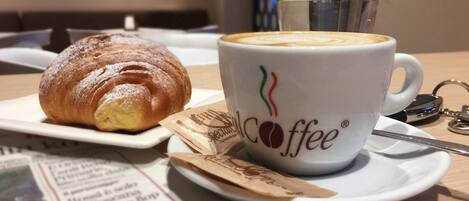 Un croissant y una taza de café con un logotipo sobre una mesa con periódicos y una cuchara.