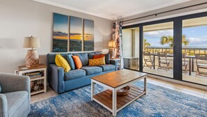 A living room with a blue sofa, a wooden coffee table, and a view of the ocean through large sliding glass doors. - Oceanfront condo w 2 pools, private balcony & beach access. Short walk to The Ritz-Carlton (Amelia Island)