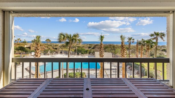 A balcony with a view of a pool and palm trees, overlooking a beach and ocean. - Oceanfront condo w 2 pools, private balcony & beach access. Short walk to The Ritz-Carlton (Amelia Island)