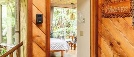 A wooden interior with a door labeled "Pahoehoe," leading to a room with a bed and a view of the outdoors.