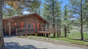 A wooden cabin with a porch and a deck, surrounded by trees. - Fireplace | Pool Table | WiFi | Hot Tub | Deer Haven (Angel Fire)
