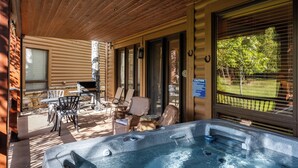 Un espacio al aire libre techado con un jacuzzi, sillas de mimbre y una mesa.