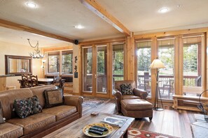 A spacious living room with a brown leather sofa, a wooden coffee table, and a large window with blinds.