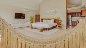 A spacious bedroom with a large bed, a ceiling fan, a view of the kitchen, and a hammock in the corner. - NOUR Villas (Belmopan)
