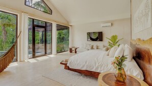 A spacious bedroom with a large bed, a hammock, and a view of lush greenery through large windows. - NOUR Villas (Belmopan)