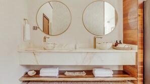 A bathroom with two round mirrors, a marble sink, and a wooden vanity. - NOUR Villas (Belmopan)