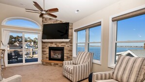 Una sala de estar con chimenea, ventilador de techo y ventanas amplias con vista al mar.
