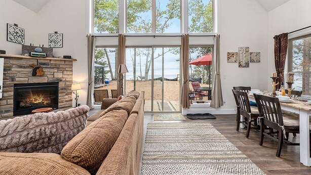 Ein geräumiges Wohnzimmer mit Kamin, großem Fenster mit Meerblick und Essbereich mit Holzsesseln.