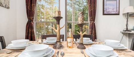 A dining table set with white plates, bowls, and cutlery, flanked by decorative tree-shaped candle holders and a bottle of champagne.