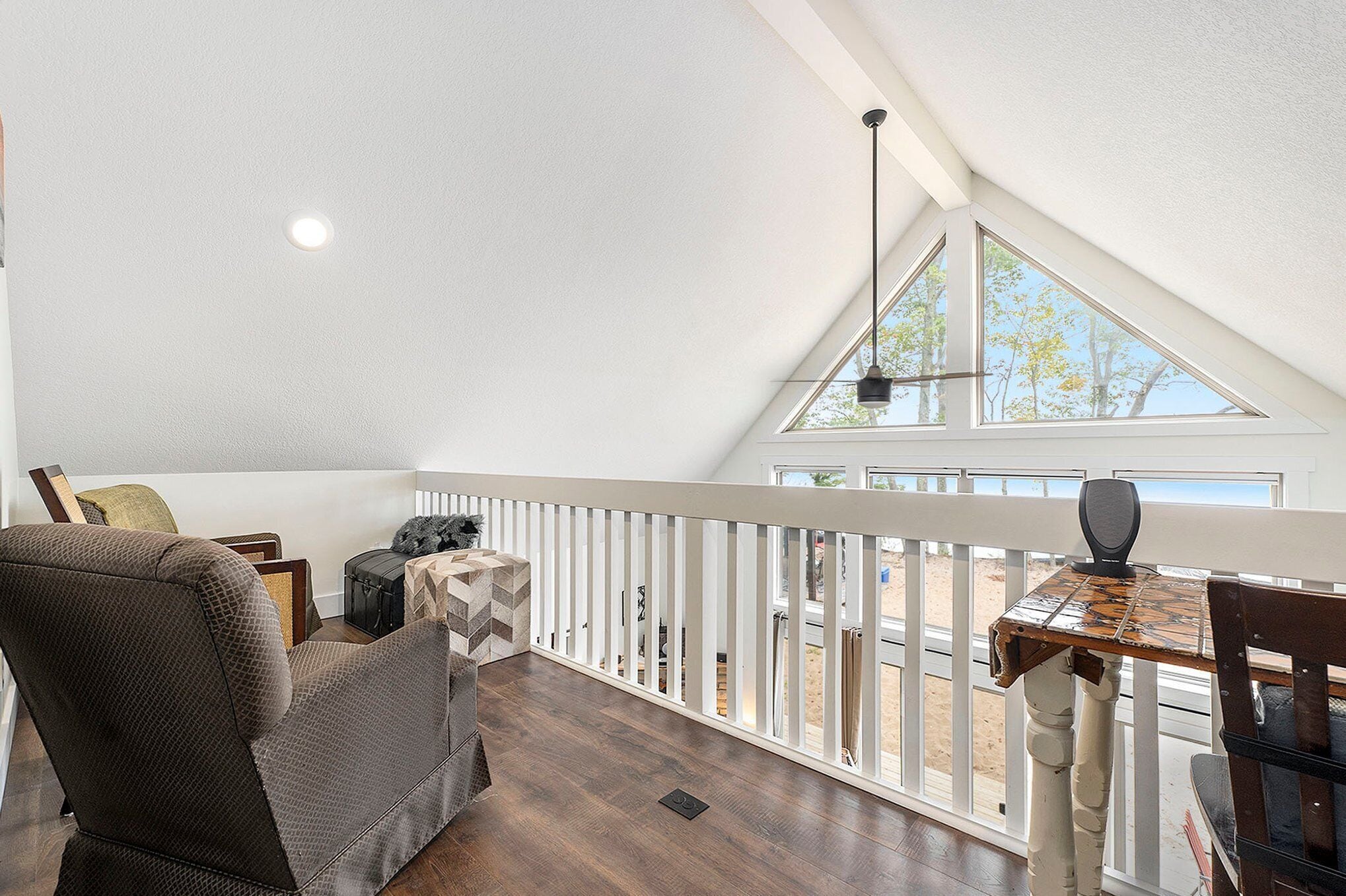 Ein Zimmer mit hohen Decken und schrägem Dach, mit Blick auf den Strand, einer Holzterrasse und einer Essecke mit Tisch und Stühlen.