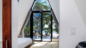 Una camera da letto con un'ampia finestra vista spiaggia, un letto e una ventola a soffitto.