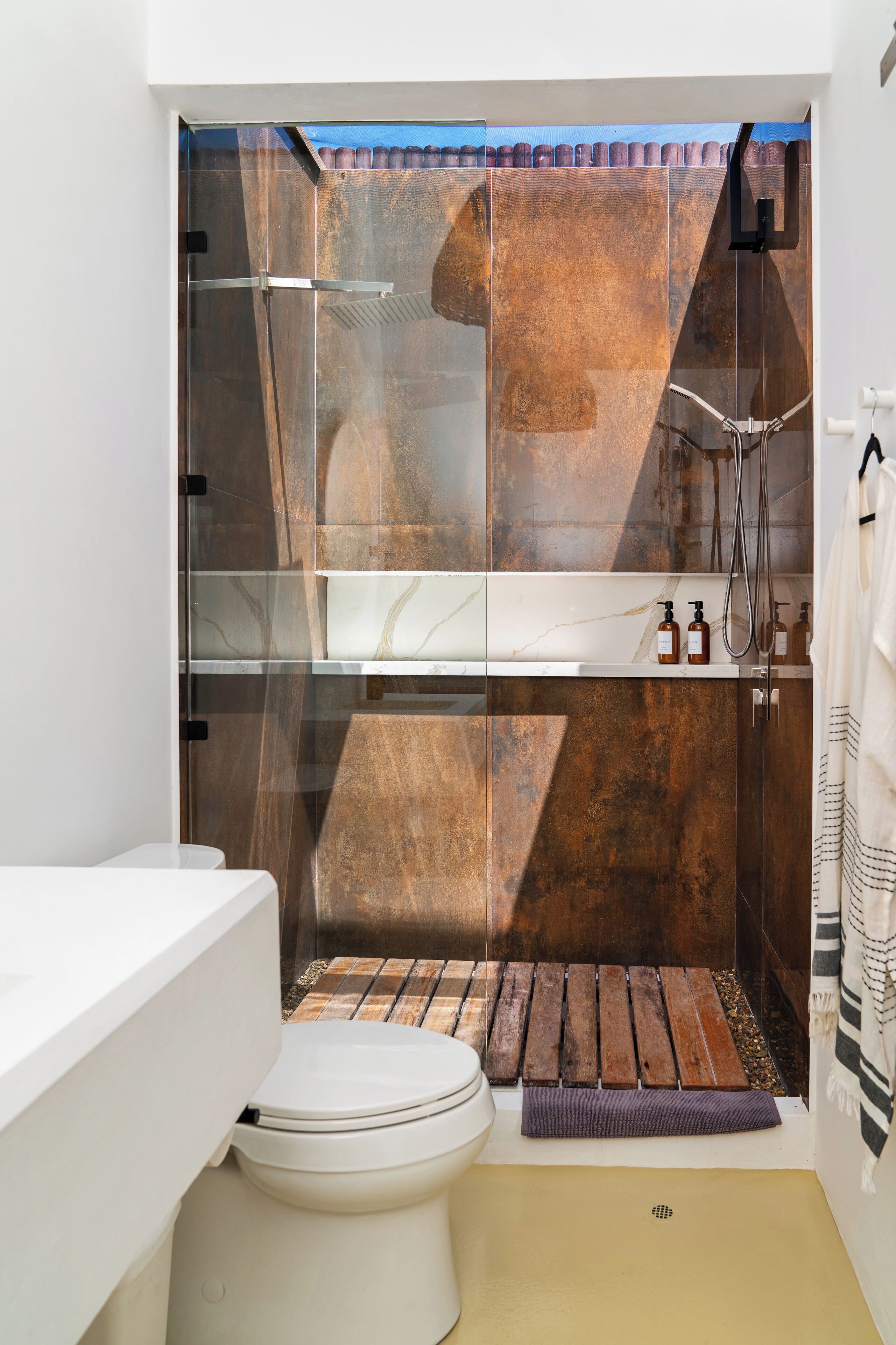 Une salle de bain moderne avec une douche à parois de verre, des toilettes blanches et un tapis de bain en bois.