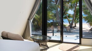 Una camera moderna con un letto, una ventola a soffitto, una porta in vetro che si apre su una vista sulla spiaggia e un tavolino.
