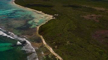 Vista aérea de la Reserva Marina Bacalar Chico, mostrando una zona costera con aguas turquesas cristalinas, una playa de arena y vegetación verde densa.