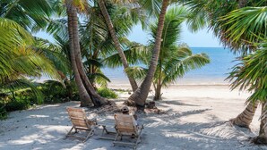 Una spiaggia con due lettini di legno sotto le palme, sabbia fine e l'oceano sullo sfondo.