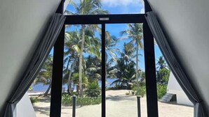 Una stanza con vista su una spiaggia e palme, tramite una finestra triangolare.