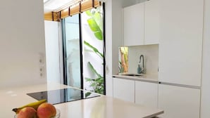 Une cuisine moderne avec un pare-feu en verre, des meubles blancs et un panier de fruits posé sur le plan de travail.